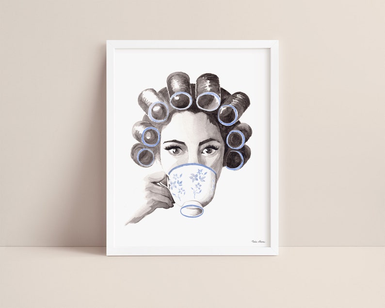 Watercolor portrait of a woman in grayscale with blue curlers in her hair sipping from a blue floral teacup. Print is displayed in a white picture frame on a blush pink background.