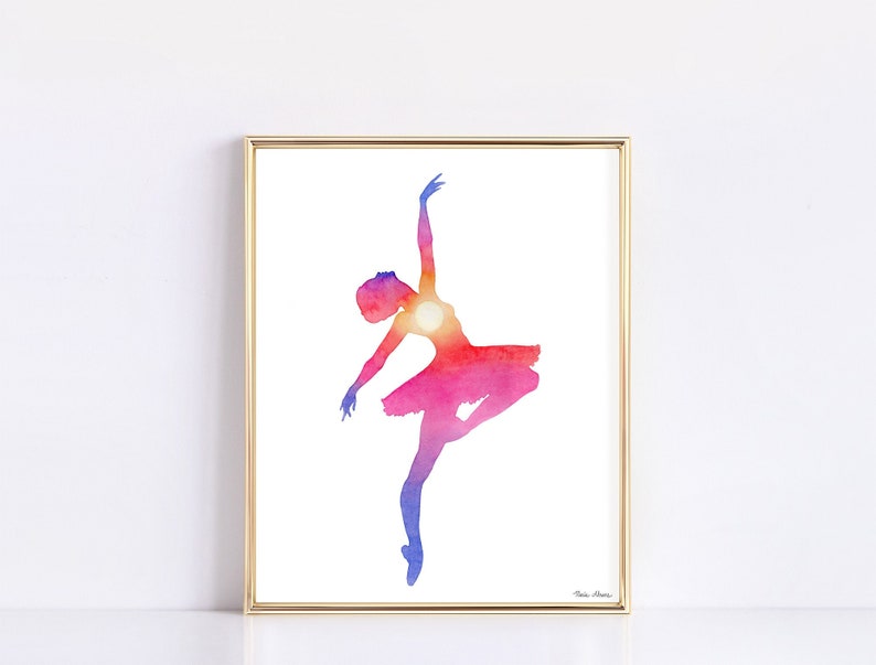 Ballerina art print featuring a silhouette painted in a double exposure style to be filled with a vibrant sunset. Watercolor print is displayed in a gold picture frame on a white background.