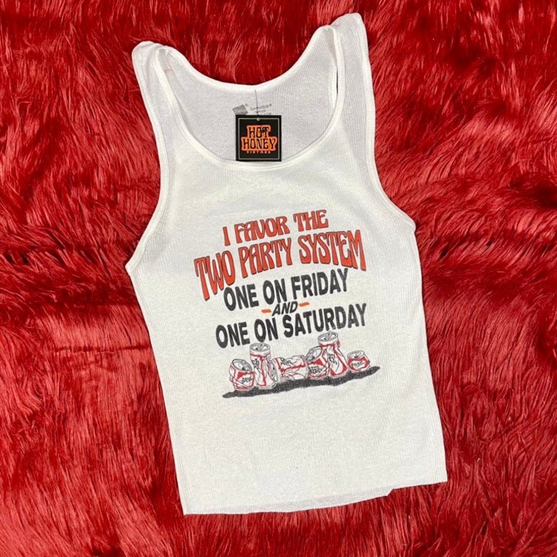 May include: White tank top with a ribbed texture. The tank top has a graphic print that says "I favour the two party system, one on Friday and one on Saturday". The graphic also includes a row of beer cans.