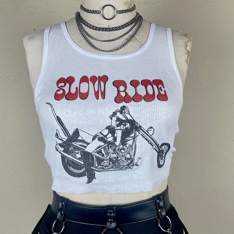 May include: White ribbed tank top with a red graphic that says "Slow Ride" and a black and white illustration of a woman riding a motorcycle.