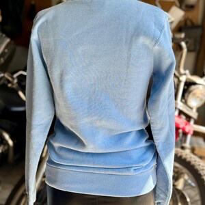 May include: A light blue sweatshirt with a crew neck and long sleeves. The back of the sweatshirt is visible, showing the soft fabric and ribbed hem. The garment is displayed on a mannequin.