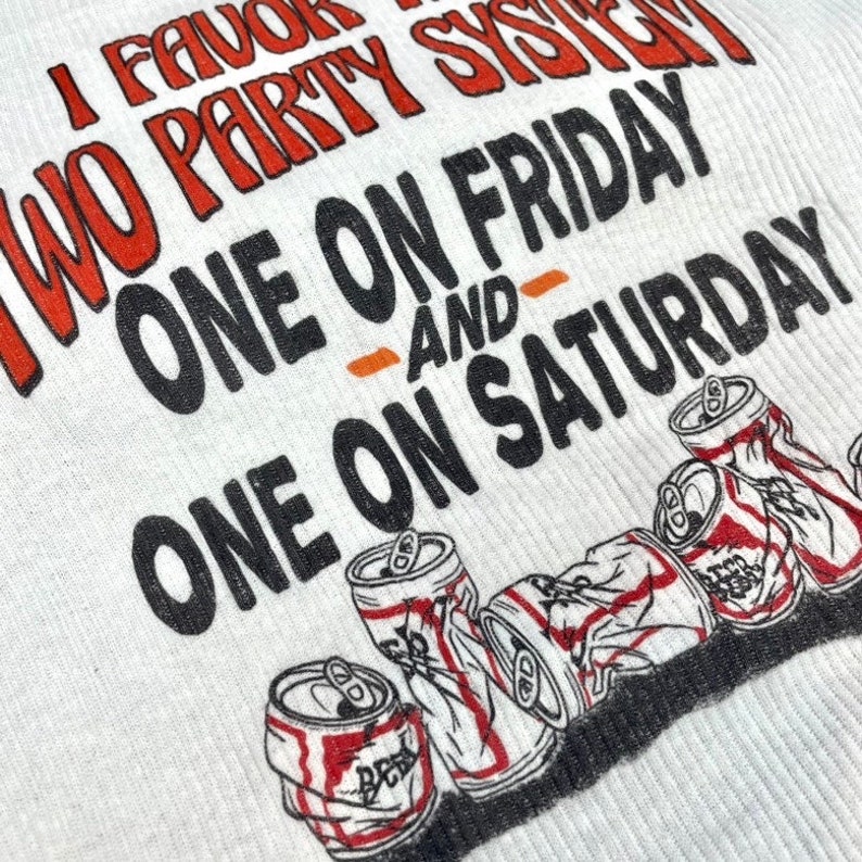 May include: White t-shirt with black text that reads "I favour a two party system - one on Friday - and - one on Saturday". The text is surrounded by images of crushed beer cans.