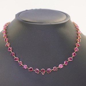 以下が含まれることがあります： 洋梨型のピンクの宝石が並んだ、繊細な金のネックレスです。