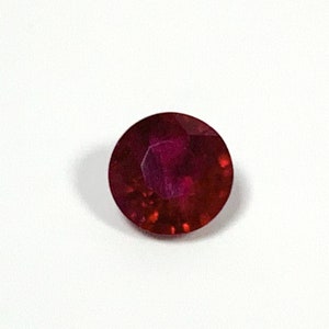 May include: A deep red gemstone with a round cut and a faceted surface.