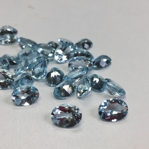May include: A collection of oval-shaped, light blue gemstones. The gemstones are faceted and have a translucent appearance.