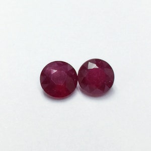May include: Two round, red ruby gemstones. The gemstones are faceted and have a polished finish.