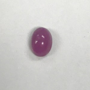 May include: A polished, oval-shaped, deep magenta gemstone. The smooth surface reflects light, creating highlights. The gem is set against a plain white background, emphasizing its color and form. This gemstone could be used in jewelry.