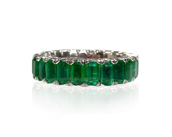 May include: A platinum emerald eternity band featuring a row of emerald-cut emeralds set in a continuous band.