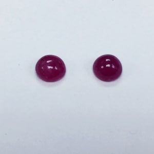 May include: Two round, red gemstones with a smooth, polished surface.