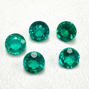 May include: Five round, faceted, green gemstones on a white background.