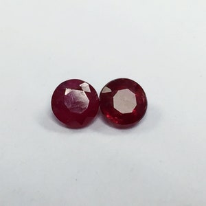 May include: Two round, red ruby gemstones. The gemstones are faceted and have a polished finish.