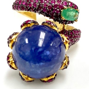 May include: A gold ring with a large blue gemstone surrounded by smaller red gemstones. The ring is designed in a snake shape with a green gemstone on the head.