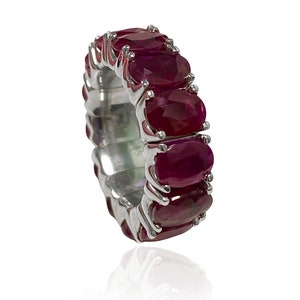 Op de afbeelding: Een zilveren ring met een rij ovale robijnen. De ring is gezet in een band van wit metaal.