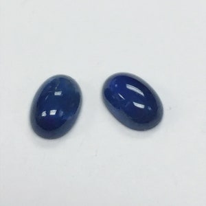May include: Two oval-shaped blue gemstones, likely sapphires, on a white background.