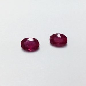 May include: Two oval-shaped ruby gemstones, each with a deep red color and a polished finish.