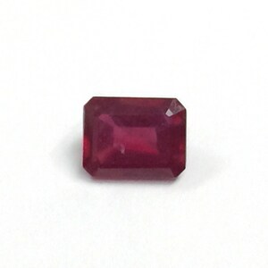 May include: A deep red emerald cut gemstone.