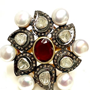 May include: A gold ring with a red gemstone surrounded by white pearls and diamonds in a floral design.