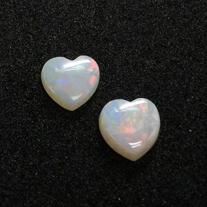 May include: Two white heart-shaped opal gemstones on a black background.
