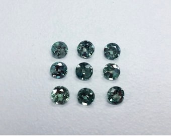 May include: Ten round, faceted gemstones in shades of green and blue. The gemstones are arranged in three rows on a white surface.
