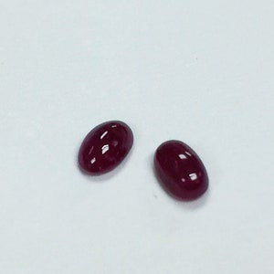 May include: Two oval-shaped, dark red gemstones on a white background.