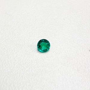 May include: A round, bright green gemstone with a faceted cut.