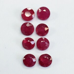 May include: Eight round, red ruby gemstones. The gemstones are faceted and have a polished finish.