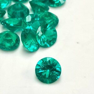 May include: A group of round, faceted, bright green gemstones, with one gemstone in the foreground.