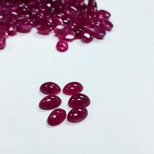 May include: A group of oval-shaped, red gemstones. The gemstones are arranged in a pile and a smaller group of eight.