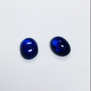 May include: Two oval-shaped blue gemstones, likely sapphires, are shown on a white background.