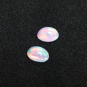 May include: Two oval-shaped white opals with iridescent rainbow colors on a black background.