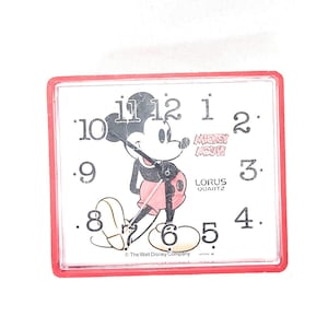 May include: Square red-framed Mickey Mouse Lorus Quartz clock. The clock face features a cartoon image of Mickey Mouse, black hands, and black numerals. The text "Mickey Mouse" and "Lorus Quartz" are also visible.