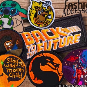 May include: A collection of iron-on patches featuring various designs, including a cartoon dog, a character from the movie Back to the Future, a dragon, a cartoon alien, and a cartoon character with a moon and the words "Stay Wild Moon Child".