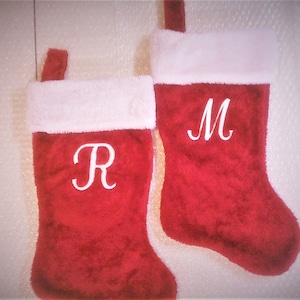 May include: Two red Christmas stockings with white fur trim. The stocking on the left has the letter "R" embroidered on it, and the stocking on the right has the letter "M" embroidered on it.