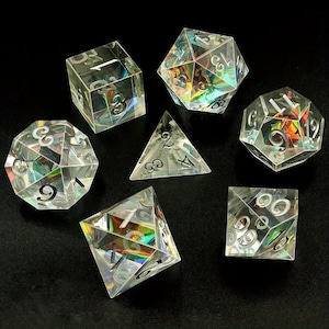 May include: Set of seven iridescent dice with black numbers. The dice are made of clear plastic with a rainbow-like sheen. The dice are a d4, d6, d8, d10, d%, d12, and d20.