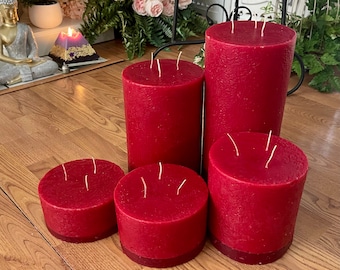 May include: Five red pillar candles of varying sizes, with multiple wicks, arranged on a wooden surface.