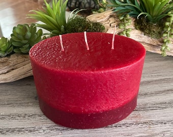 May include: A large, oval-shaped, red candle with a textured surface and four wicks. The candle has a darker red band around the bottom.