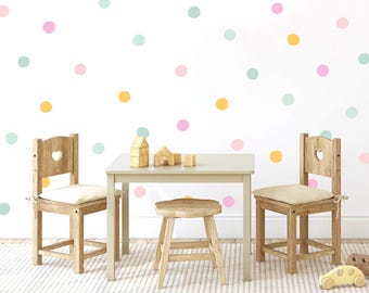 May include: A white wall with pastel pink, light blue and yellow polka dots. Two wooden chairs with heart-shaped cutouts in the backrests are placed either side of a small wooden table. A small wooden stool is in front of the table.