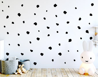 May include: A white wall decorated with black polka dots. Two gray fabric storage baskets sit on a wooden floor, with two stuffed teddy bears inside. A white bunny-shaped lamp is on the right.