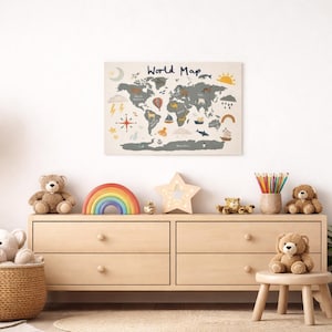 Könnte beinhalten: Eine beige Holzkommode mit einem Weltkarten-Druck darüber. Die Karte zeigt Illustrationen von Booten, Heißluftballons und anderen reisebezogenen Bildern. Die Kommode ist mit Teddybären, einem Regenbogen und einem sternförmigen Licht dekoriert.