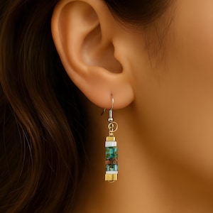 Könnte beinhalten: Hängeohrringe mit einem silbernen Haken und einem rechteckigen Design. Die Ohrringe weisen abwechselnd goldene, weiße, türkisfarbene und braune rechteckige Perlen auf. Der Text "Lucy - Matching Earrings" ist sichtbar.
