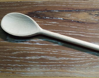 May include: A wooden spoon with a light brown color and a smooth surface. The spoon is lying on a wooden surface with a light brown color and a grain pattern.