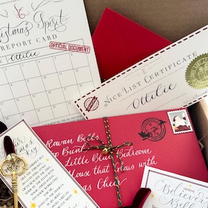 Pode incluir: Uma caixa de presente de Natal com um envelope vermelho, uma chave, um sino e um cart&atilde;o que diz "Rowan Bells Top Bunk Little Blue Bedroom House that Glous with as Cheer". O cart&atilde;o &eacute; decorado com um cord&atilde;o verde e dourado. A caixa est&aacute; cheia de papel picado.