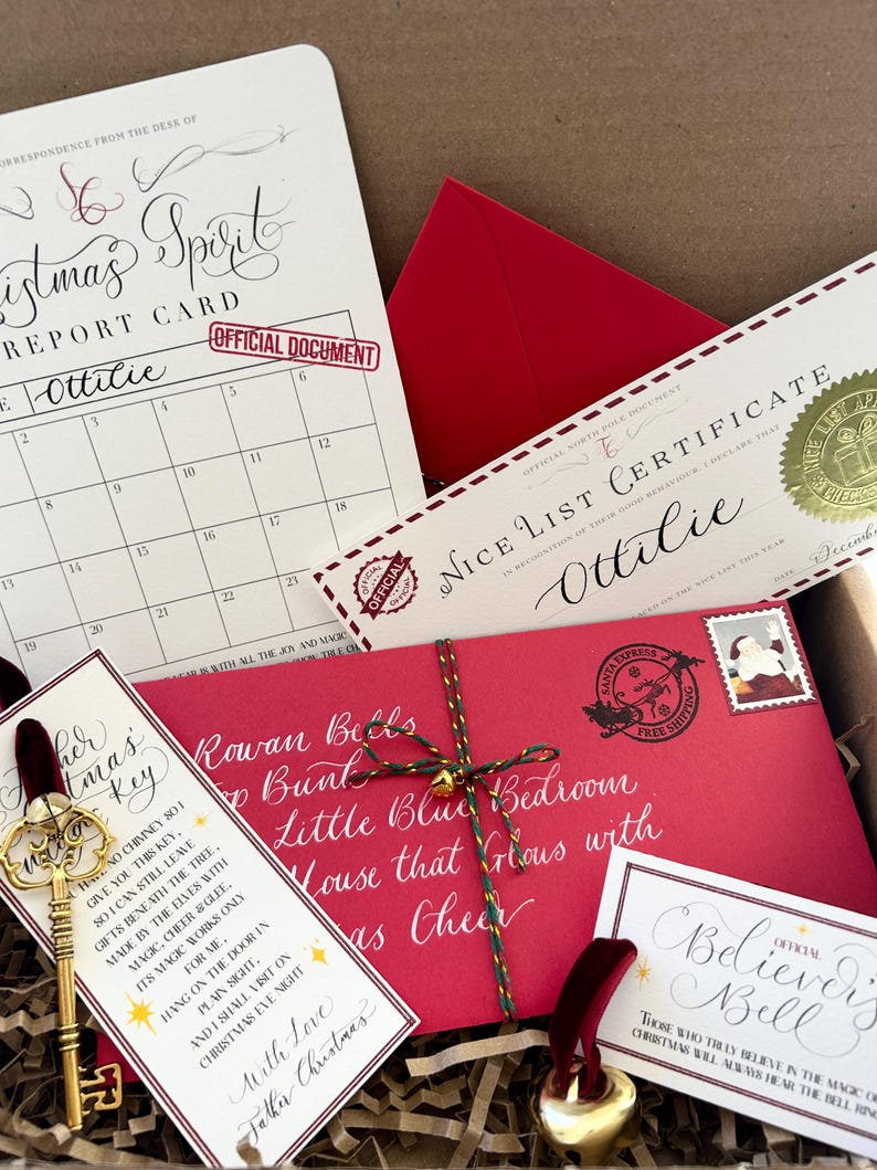 Pode incluir: Uma caixa de presente de Natal com um envelope vermelho, uma chave, um sino e um cart&atilde;o que diz "Rowan Bells Top Bunk Little Blue Bedroom House that Glous with as Cheer". O cart&atilde;o &eacute; decorado com um cord&atilde;o verde e dourado. A caixa est&aacute; cheia de papel picado.