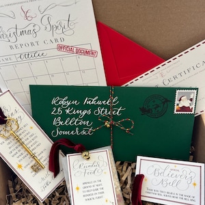 Pode incluir: Uma caixa de presente de Natal com um envelope verde endere&ccedil;ado a Robyn Inkwell, 25 Kings Street, Bellton, Somerset. A caixa cont&eacute;m uma chave de ouro, um pequeno saco de comida para renas, um sino de ouro e um cart&atilde;o que diz "Official Believers Bell".