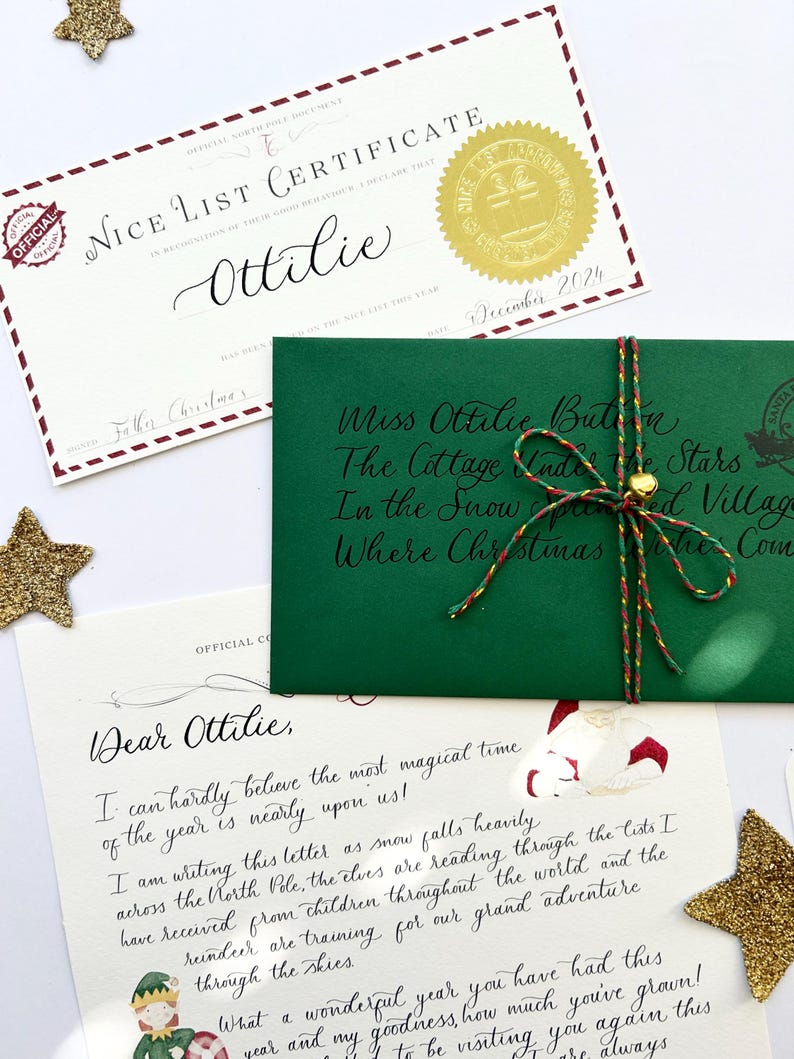 Pode incluir: Um envelope verde com um selo dourado e uma corda vermelha e branca amarrada ao redor. O envelope &eacute; endere&ccedil;ado a Miss Ottilie Button, The Cottage Under the Stars, In the Snow,  Spiced Village, Where Christmas Wishes Come. Uma carta escrita &agrave; m&atilde;o com um desenho do Papai Noel e um duende &eacute; vis&iacute;vel na mesa ao lado do envelope.