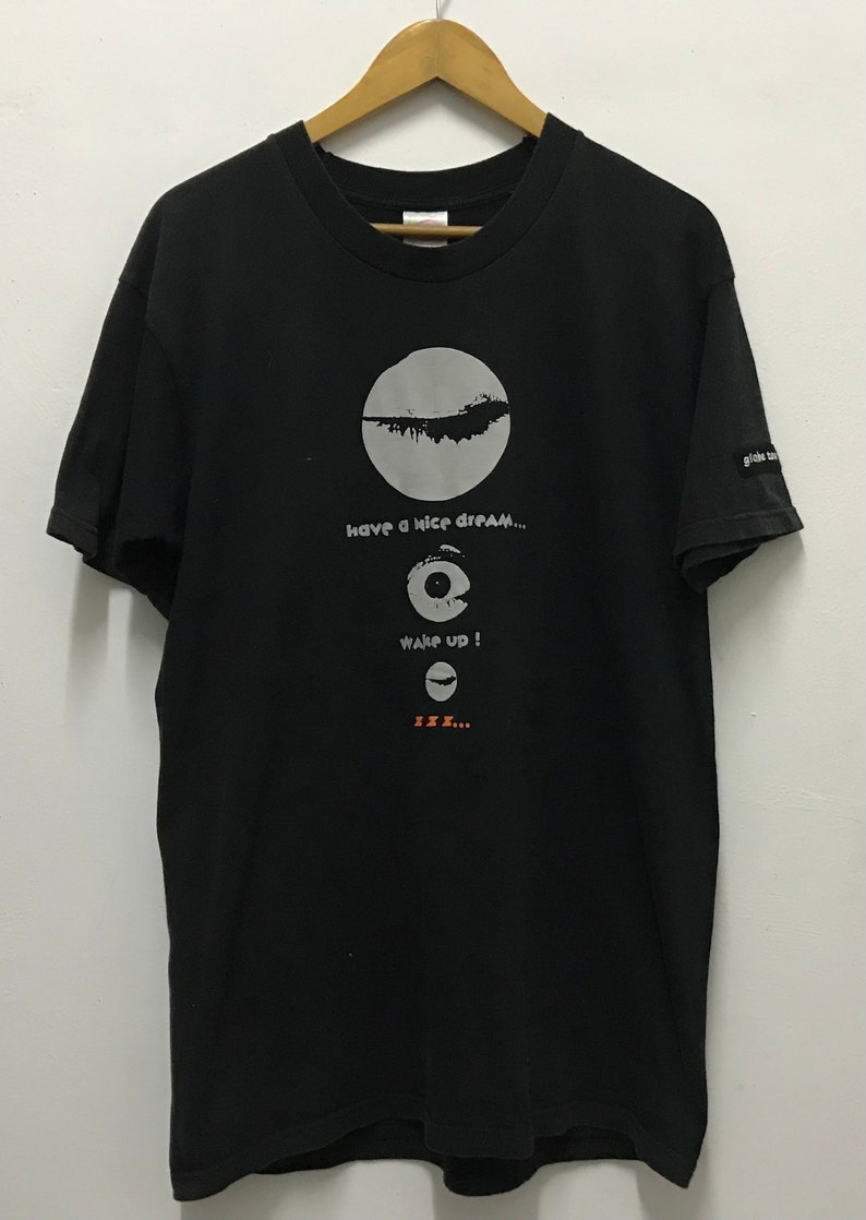 Peut inclure: T-shirt noir avec un motif blanc en forme de cercle avec une ligne qui le traverse, et le texte "have a nice dream...", "wake up!" et "zzz..."