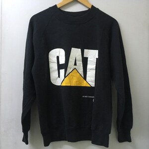 May include: Black long-sleeve sweatshirt with a white "CAT" logo and a yellow triangle. The text "&copy;1992 Caterpillar" is printed below the logo.
