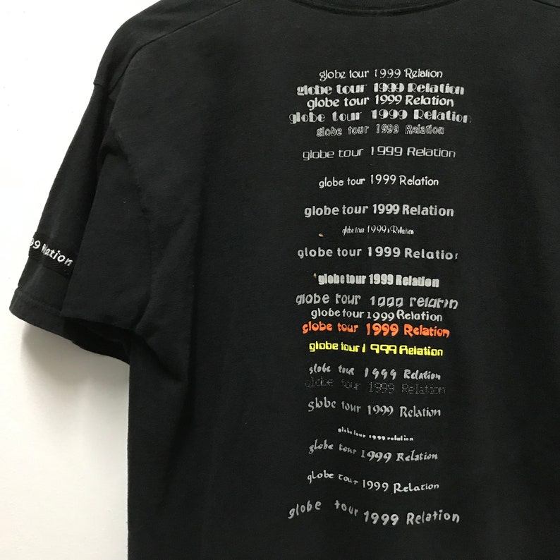Peut inclure: T-shirt noir avec le texte "globe tour 1999 Relation" r&eacute;p&eacute;t&eacute; plusieurs fois en blanc, orange et jaune.