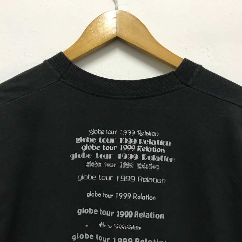 Peut inclure: T-shirt noir avec le texte "globe tour 1999 Relation" r&eacute;p&eacute;t&eacute; plusieurs fois dans un design empil&eacute;.