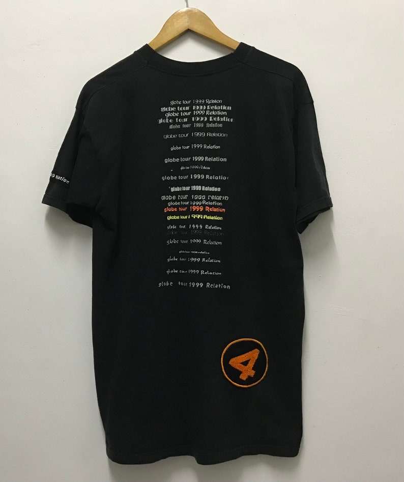 Peut inclure: T-shirt noir avec un grand chiffre 4 orange en bas &agrave; droite. Le dos du t-shirt porte le texte "globe tour 1999 Relation" r&eacute;p&eacute;t&eacute; plusieurs fois dans diff&eacute;rentes couleurs et polices.